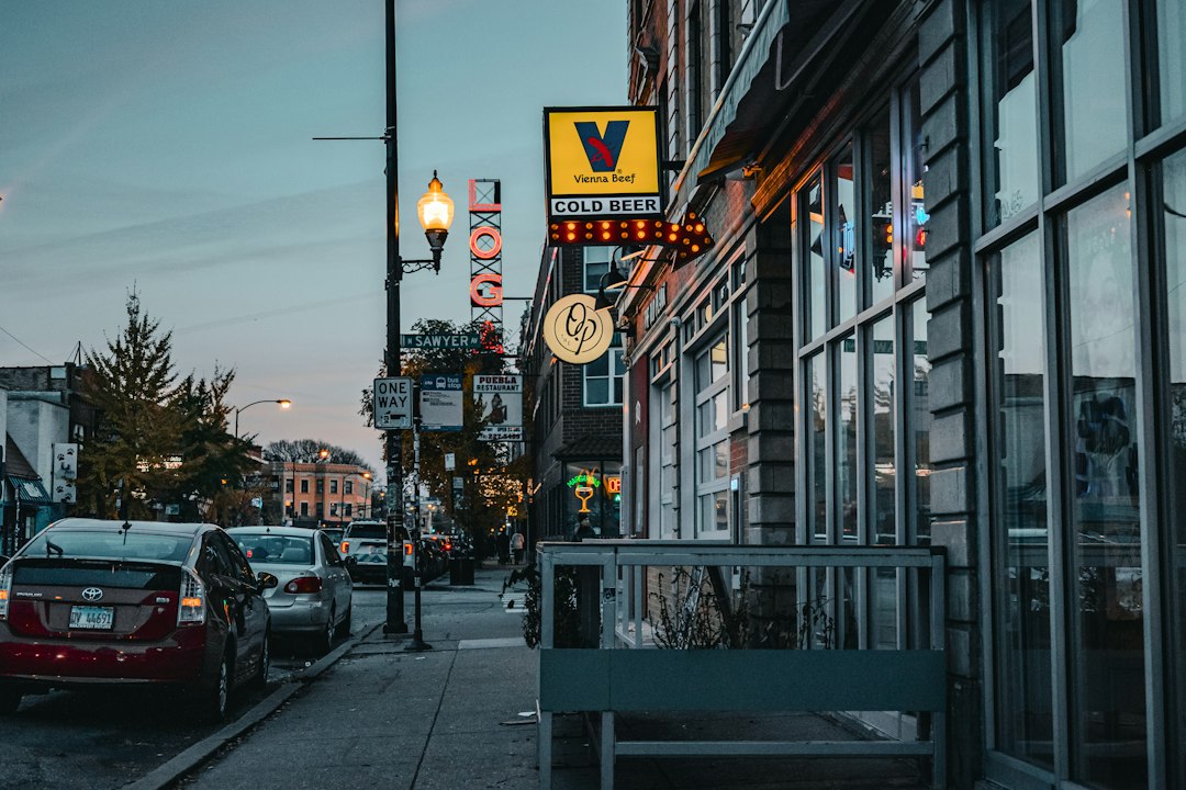 A charming and brightly lit small business storefront stands out on a city street at dusk, representing a local Stuart shop thriving against larger competitors.