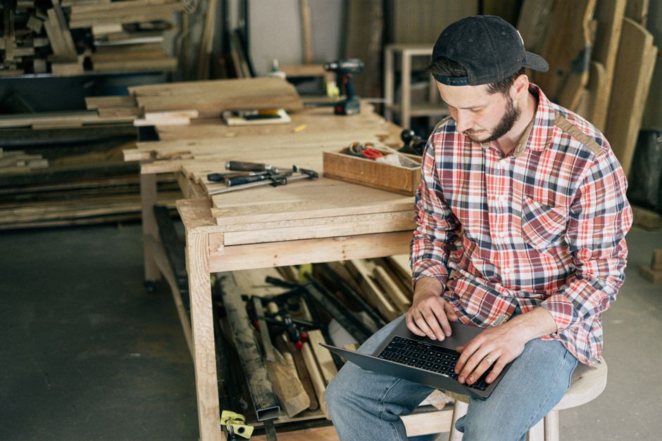 A focused artisan in a clean, modern workshop uses a laptop, symbolizing a small business leveraging technology to enhance their craft and compete.