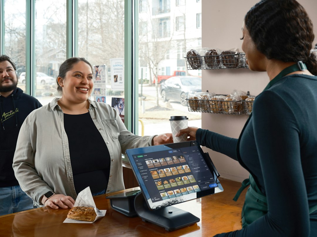Friendly small business owner in a bright, modern cafe uses a tablet, illustrating the integration of accessible AI tools ...
